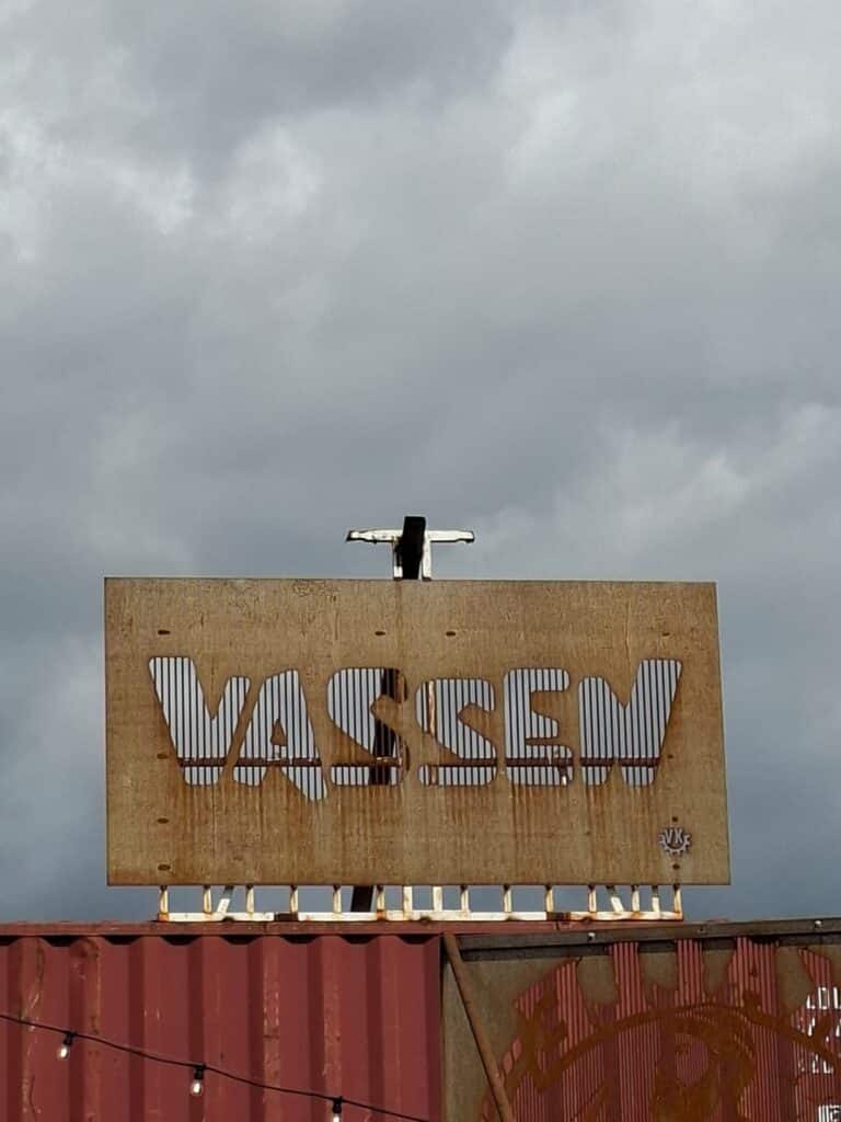 Skylten VASSEN monterad ovanpå en containerbyggnad, sedd underifrån mot molnig himmel.